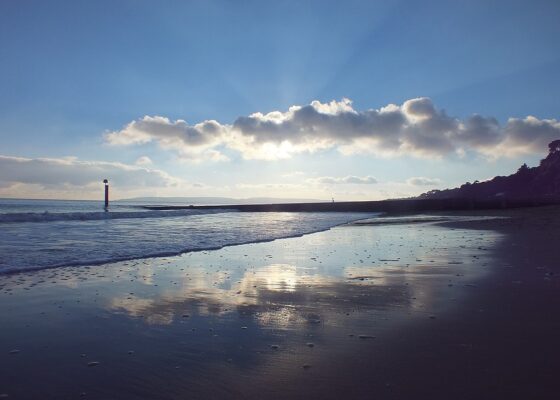 Beach sunrise with blue sky, clouds, a calm ocean wave and small lighthouse