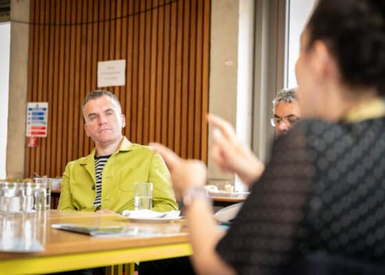 White man sitting attentively at a table in a yellow jacket